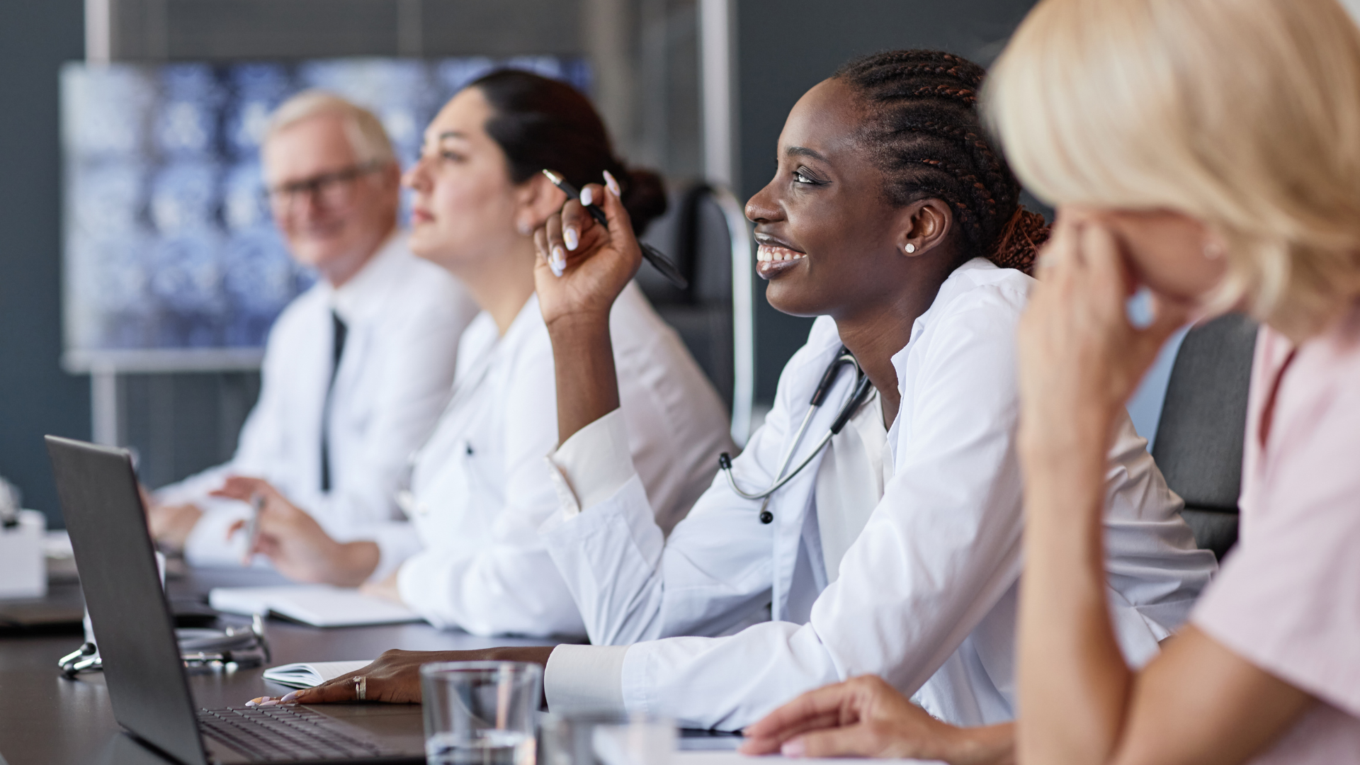Side view of positive African American female clinician asking colleague follow up question after presentation in group seminar while sitting at table in medical office, copy space