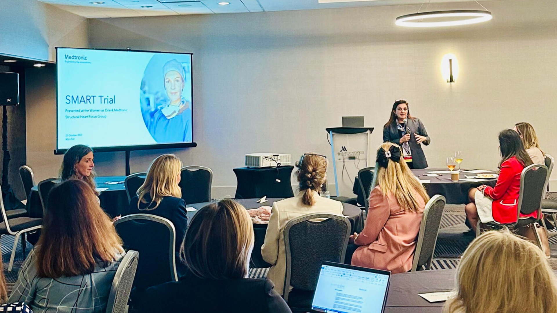 A Women As One talk on producing a SMART trial, with physicians sat round tables looking at Women As One's founder. Dr. Roxana Mehran