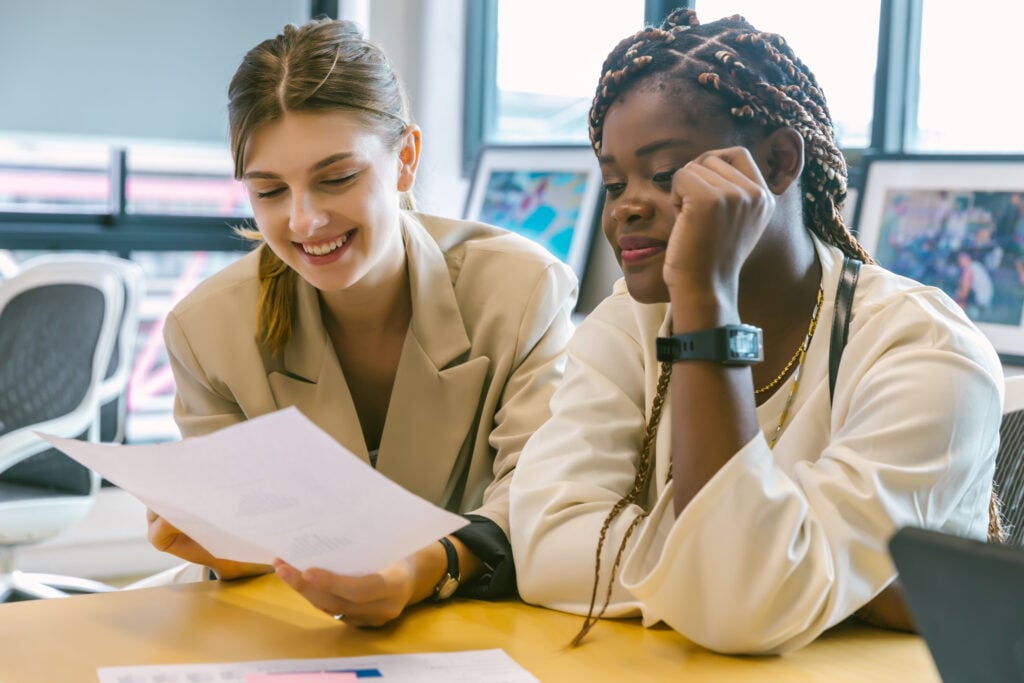 Two young adult women at a desk reading a piece of paper