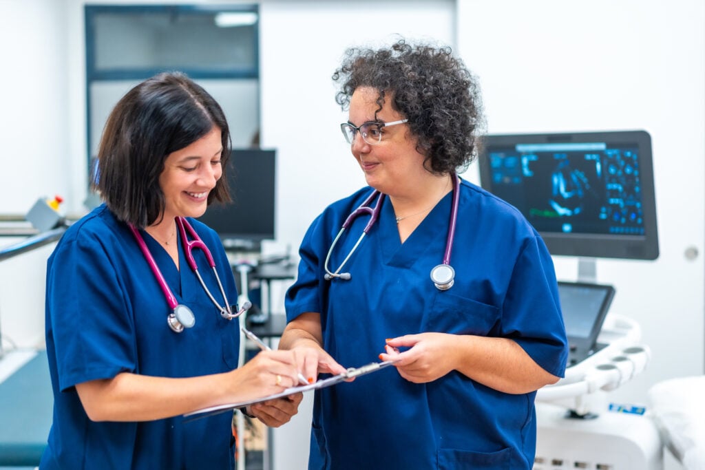 Two women physicians smiling and discussing documents in a hospital setting
