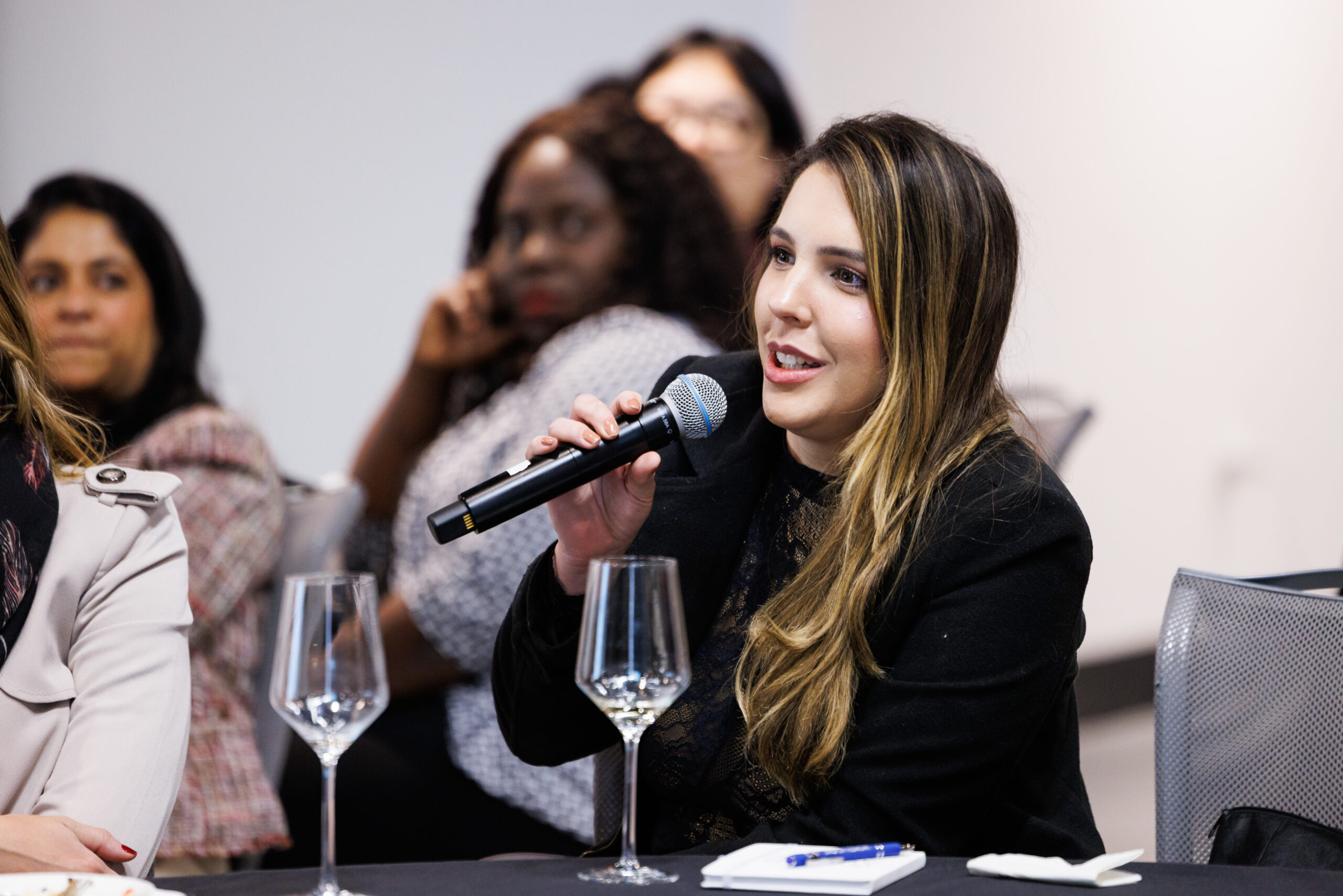 For Partners 10 Woman sat at a table during an event speaking into a microphone